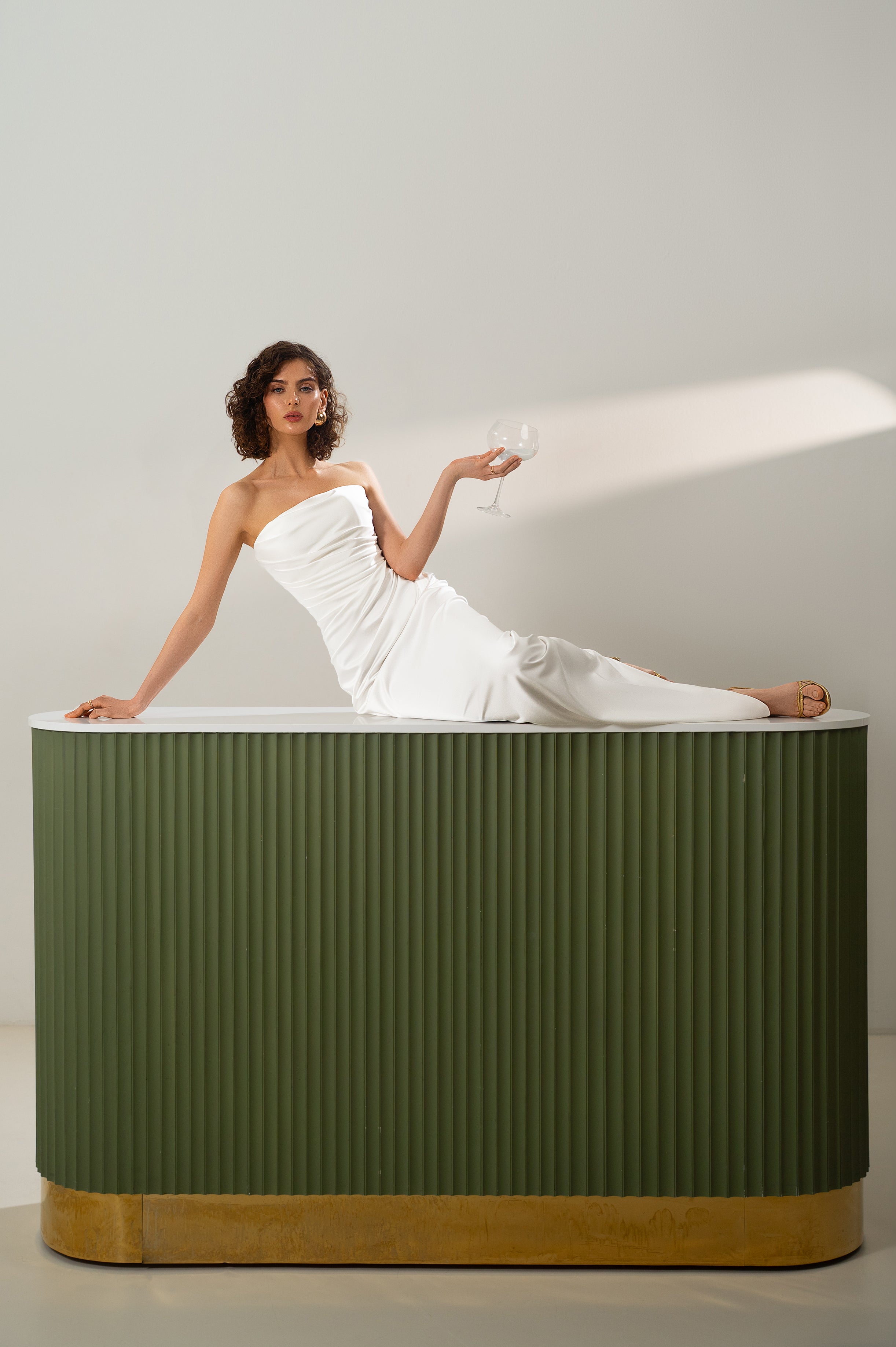 Woman in a white dress sitting  against a plain background